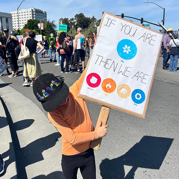 A kid holding up a protest sign  thats says "IF YOU ARE [ice] THEN WE ARE [fighting] [fire] [rock] [steel]" with symbols instead of words for the types. In Pokemon, Ice type are weak to Fighting, Fire, Rock, and Steel types.