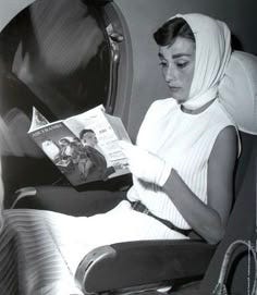 This may contain: a woman reading a magazine while sitting in an airplane with her head covering over her face