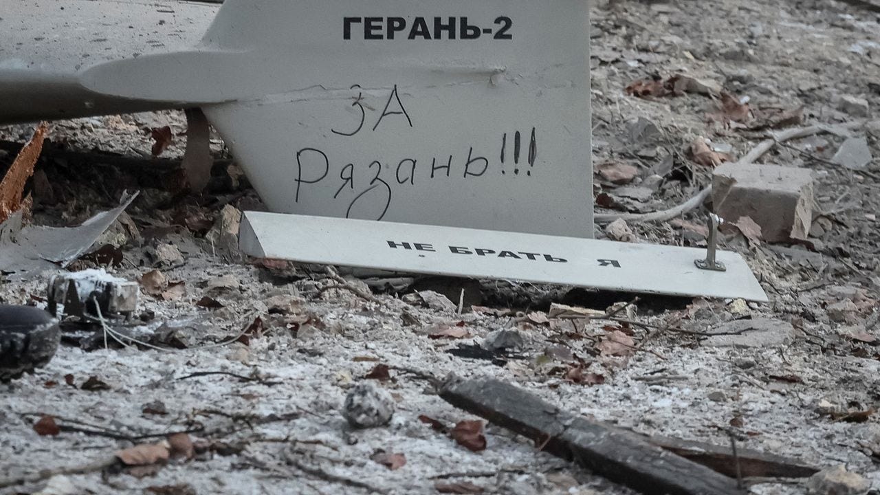 Grey tail fin of a crashed drone marked GERAN-2 in Cyrillic, lying in rubble and dead leaves