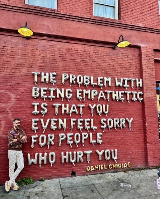 A red painted brick wall has balloon writing that reads 'theproblem with being empathetic is that you even feel sorry for people who hurt you - Daniel Chioac'