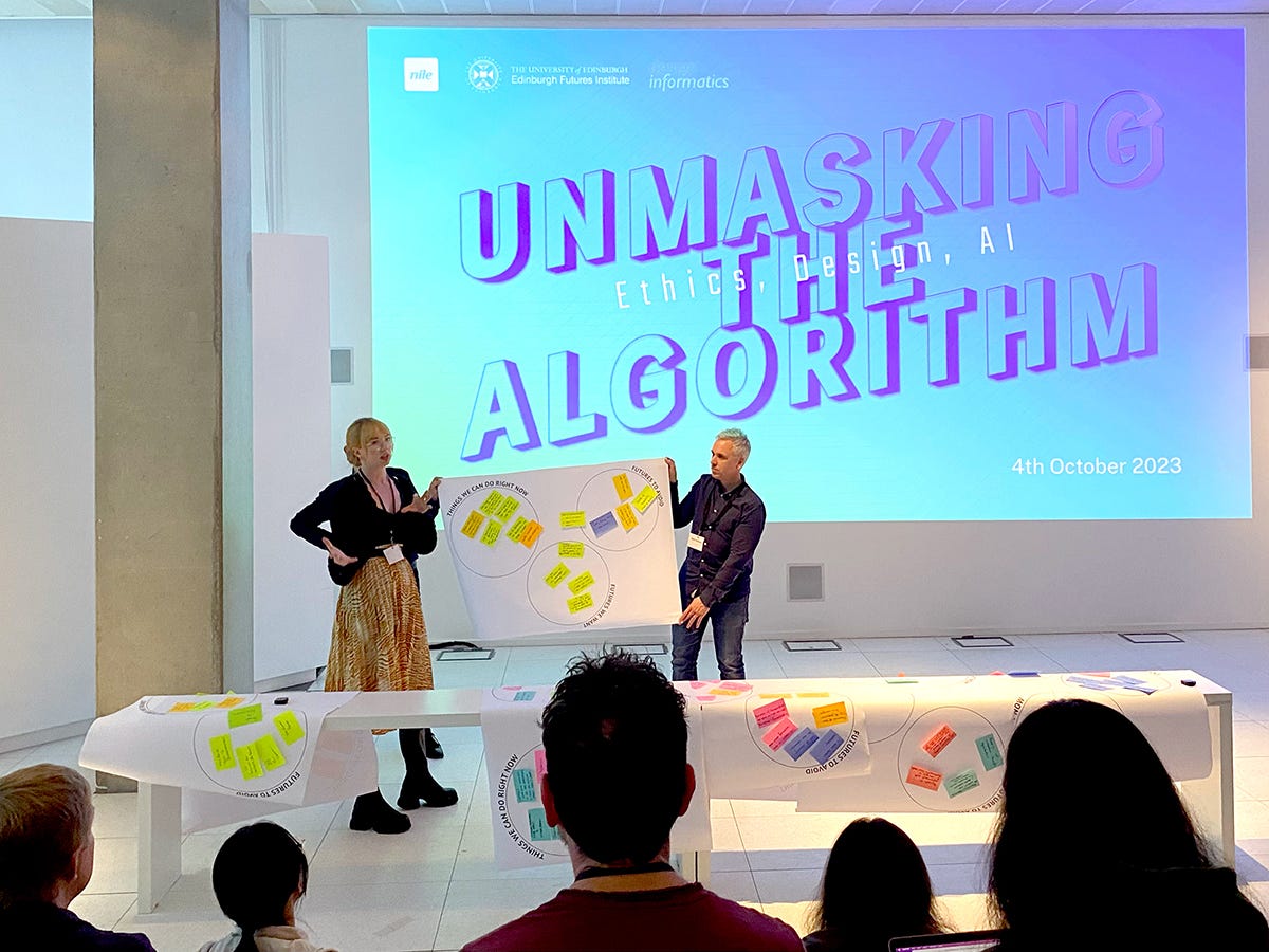 A woman and a man holding up a poster covered in post-it notes in front of an audience