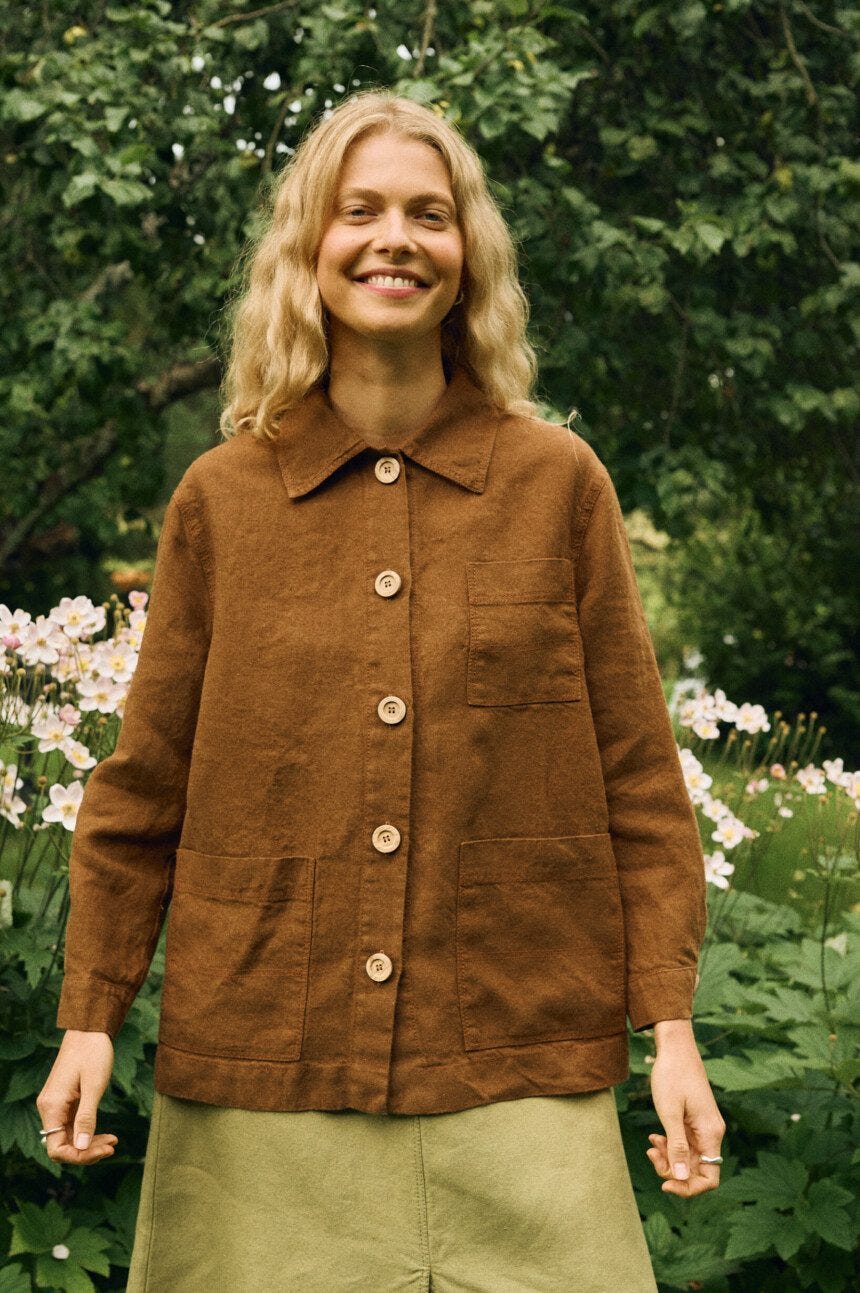 Close-up of a warm brown linen-wool jacket featuring a pointed collar, front button closure, and three patch pockets, paired with a heavy-weight olive green linen skirt