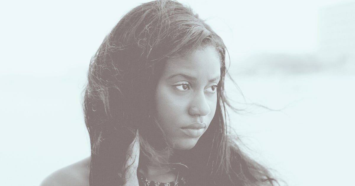 a pensive young woman looks into the distance, unsmiling