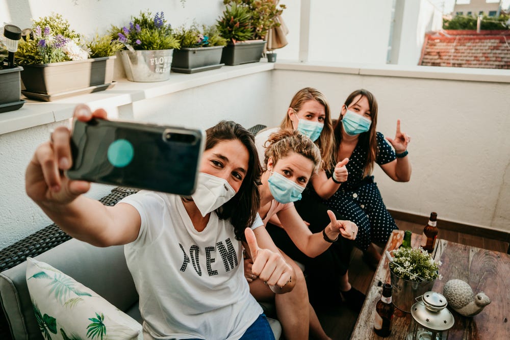 Group of young girlfriends meeting after the quarantine caused by the covid19. Taking precaution with surgical masks and taking photos together with a smartphone. Group of young girlfriends meeting after the quarantine caused by the covid19. Taking precaution with surgical masks and taking photos together with a smartphone.