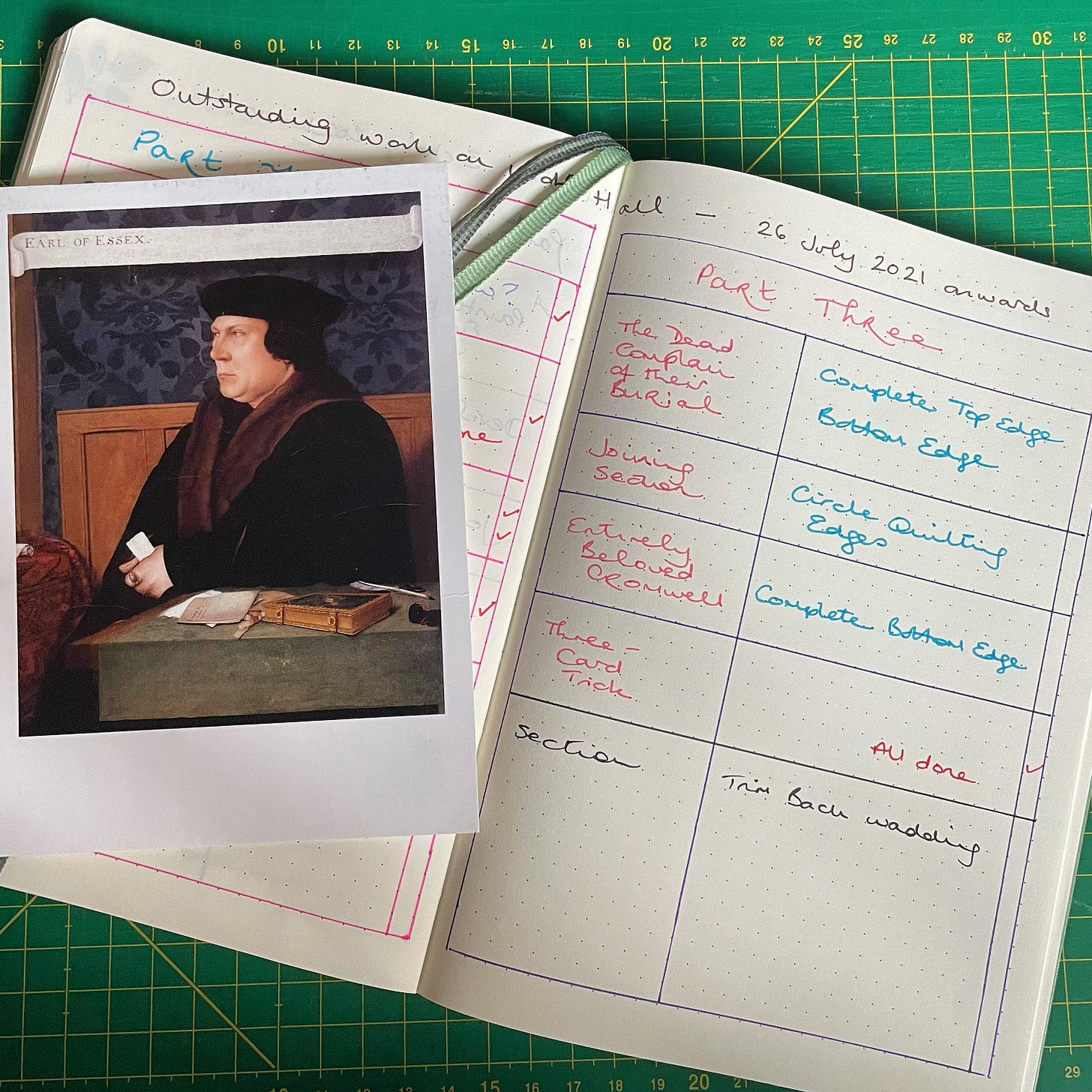 A notebook showing a table of tasks to be completed to finish the Wolf Hall Quilt. A postcard of Thomas Cromwell is laid on top.