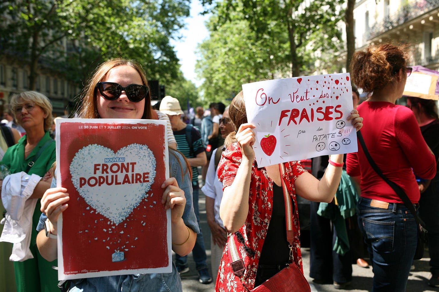 Two attendees of a march hold up signs, one with a white heart emblazoned with "Nouveau Front Populaire" Two attendees of a march hold up signs, one with a white heart emblazoned with "Nouveau Front Populaire"