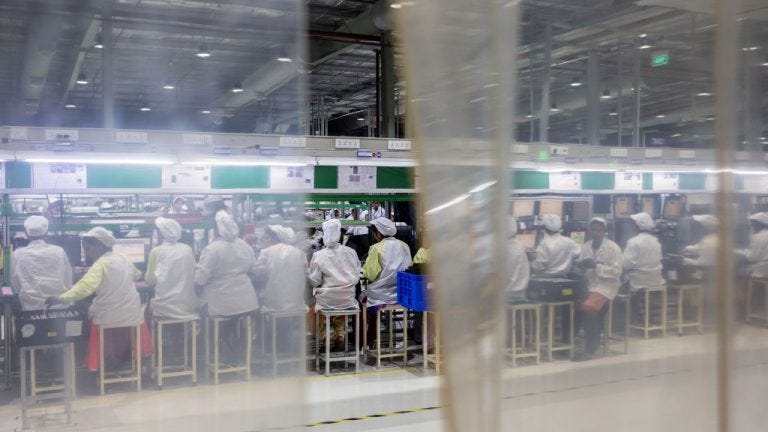 A view of a factory workspace showing several employees seated at workstations, wearing protective clothing and head coverings, with the environment partially obscured by a transparent air curtain.