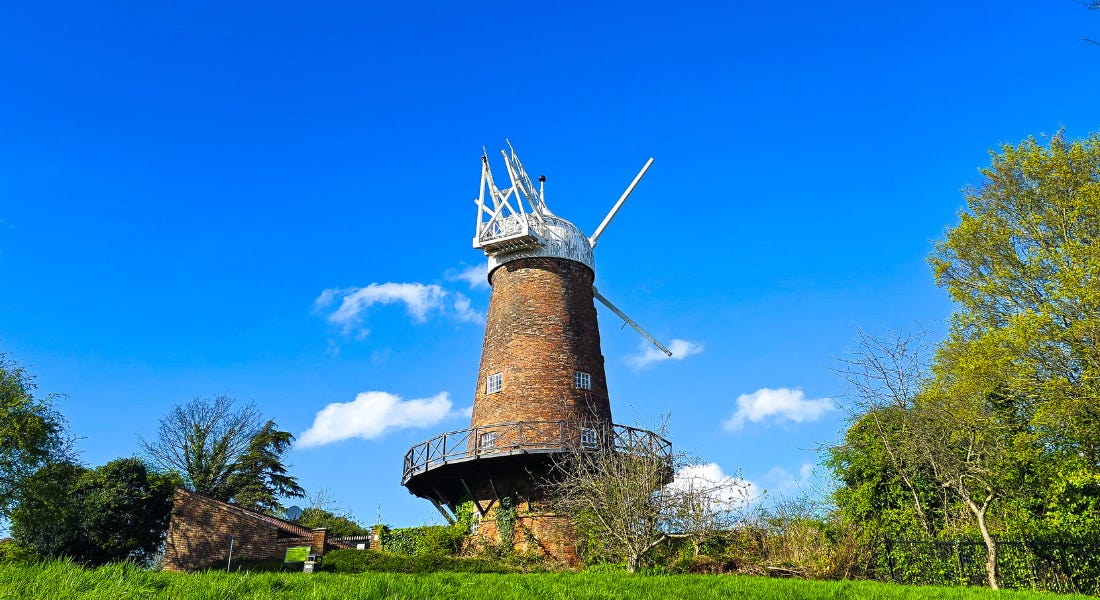 A windmill with a blue sky behind it and a lawn in front of it A windmill with a blue sky behind it and a lawn in front of it