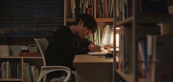 This may contain: a man sitting at a desk in front of a book shelf