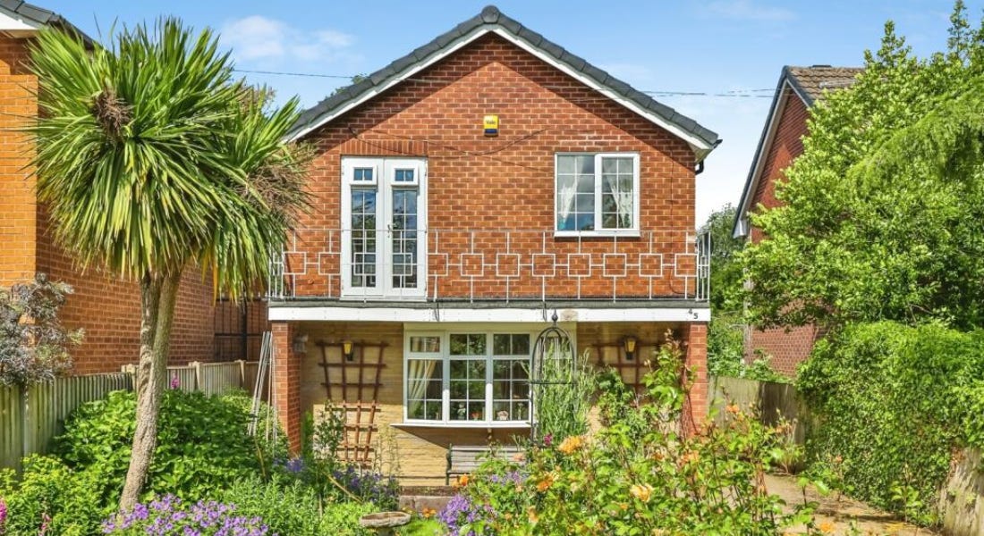 A house with a brick exterior and windows, and a landscaped garden with trees and flowers outside it