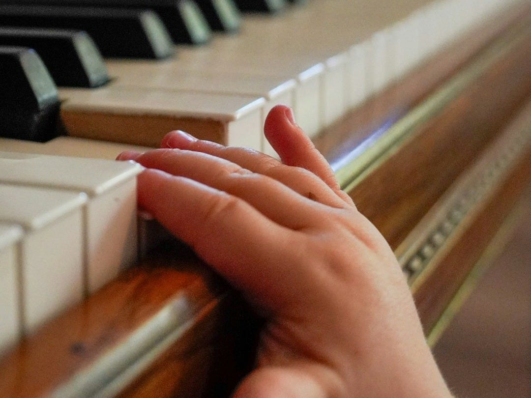 A child's hand rests on a piano keyboard. A child's hand rests on a piano keyboard.