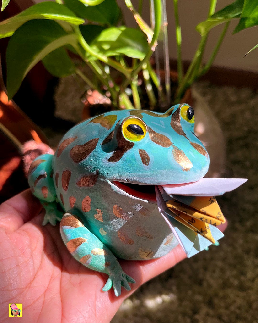 Annie holding the clay frog with origami fly placed halfway inside the frog's mouth.