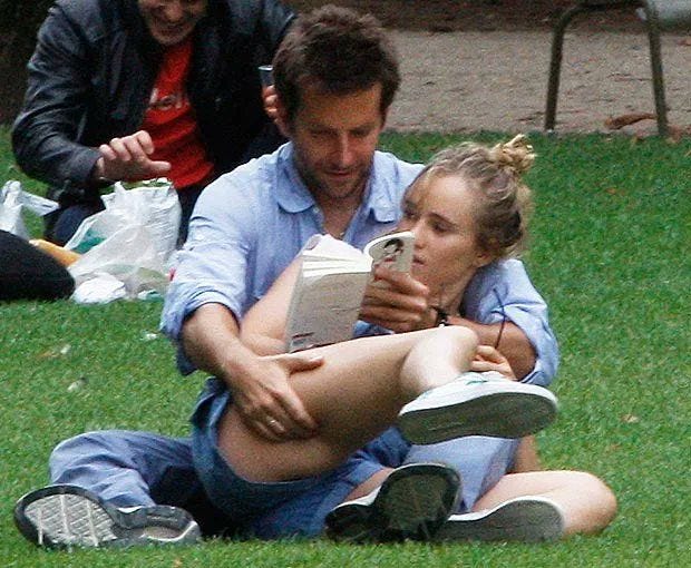 This may contain: a man and woman sitting on the grass reading