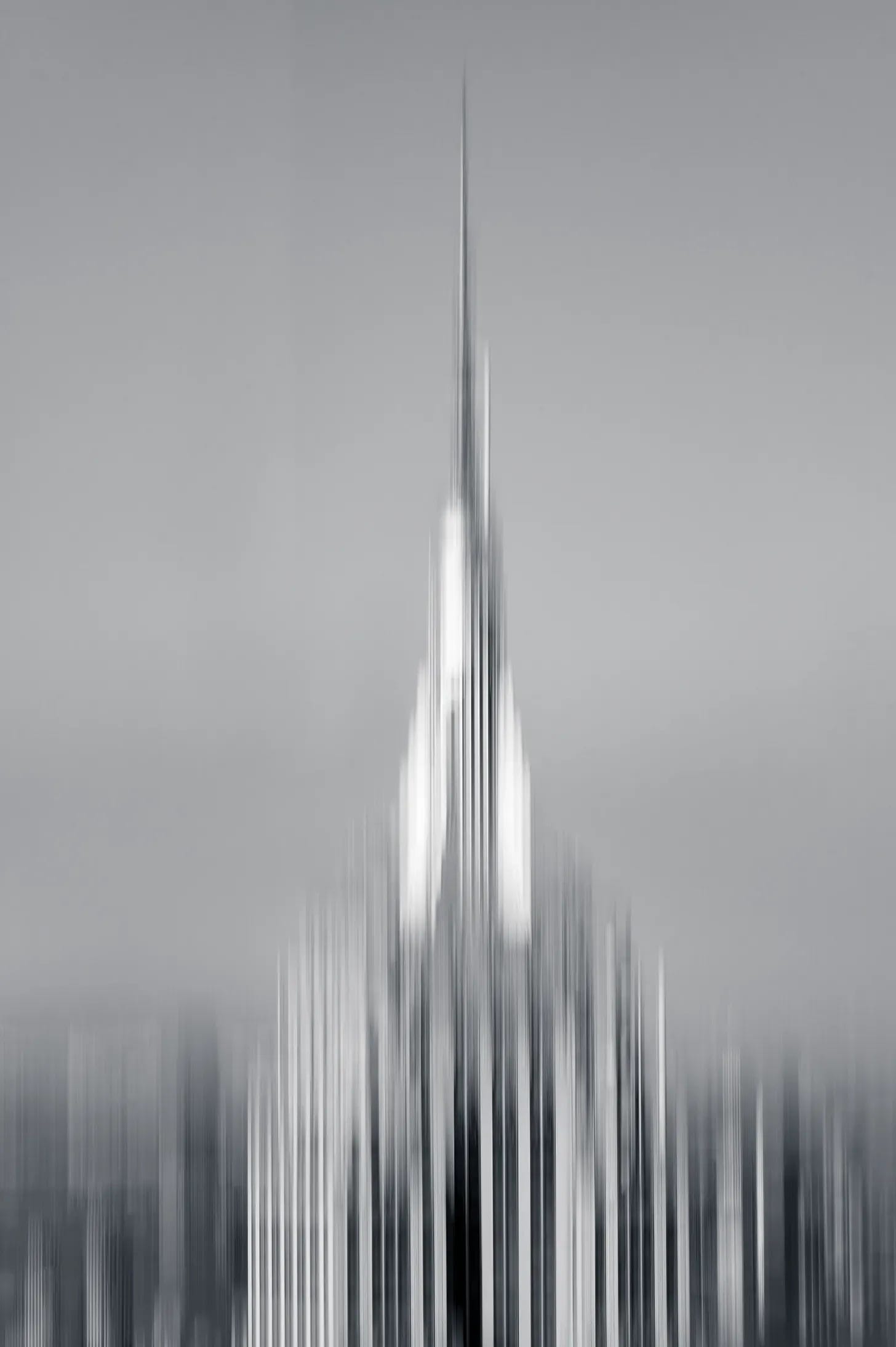A tall spire dissolved into fine vertical streaks by a moving camera, the buildings beneath it pulled into pale ribbons, in black and white. A tall spire dissolved into fine vertical streaks by a moving camera, the buildings beneath it pulled into pale ribbons, in black and white.
