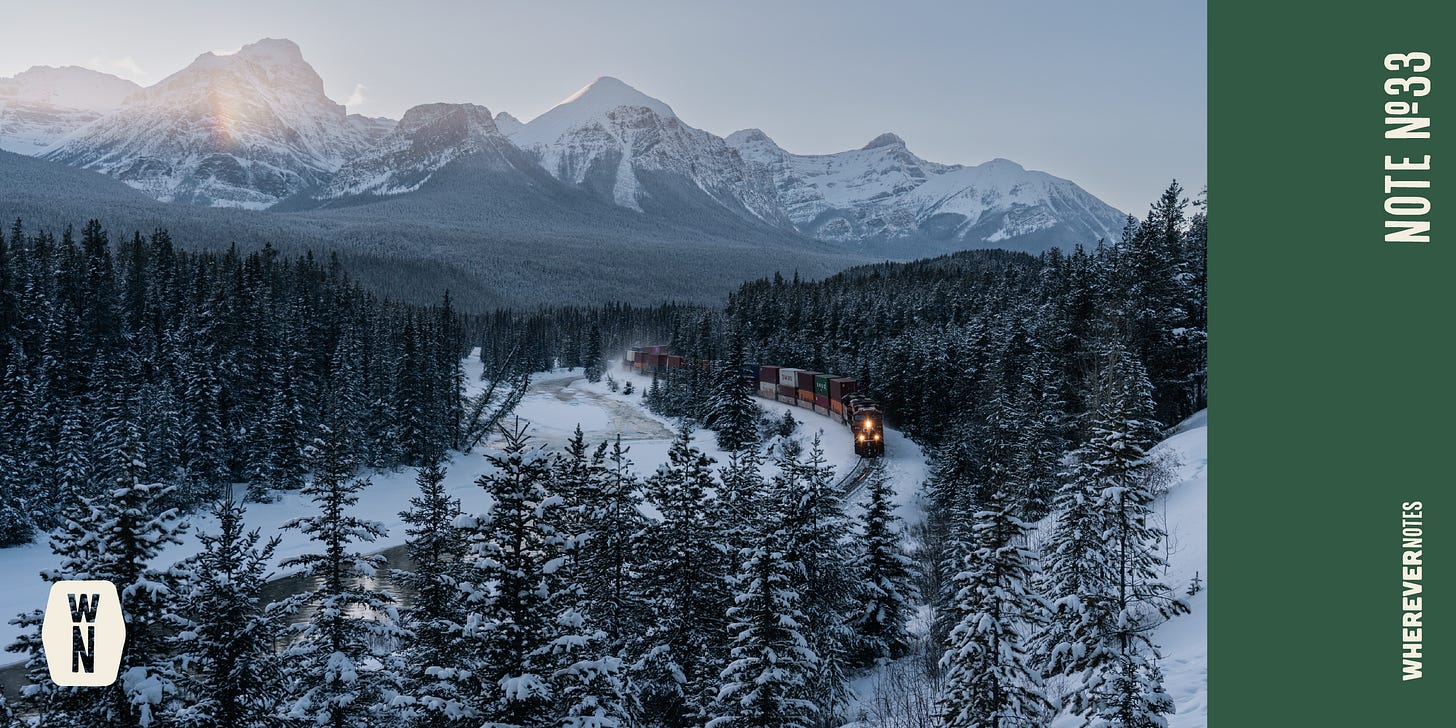 Train carving through pines and snow underneath the mountains. 