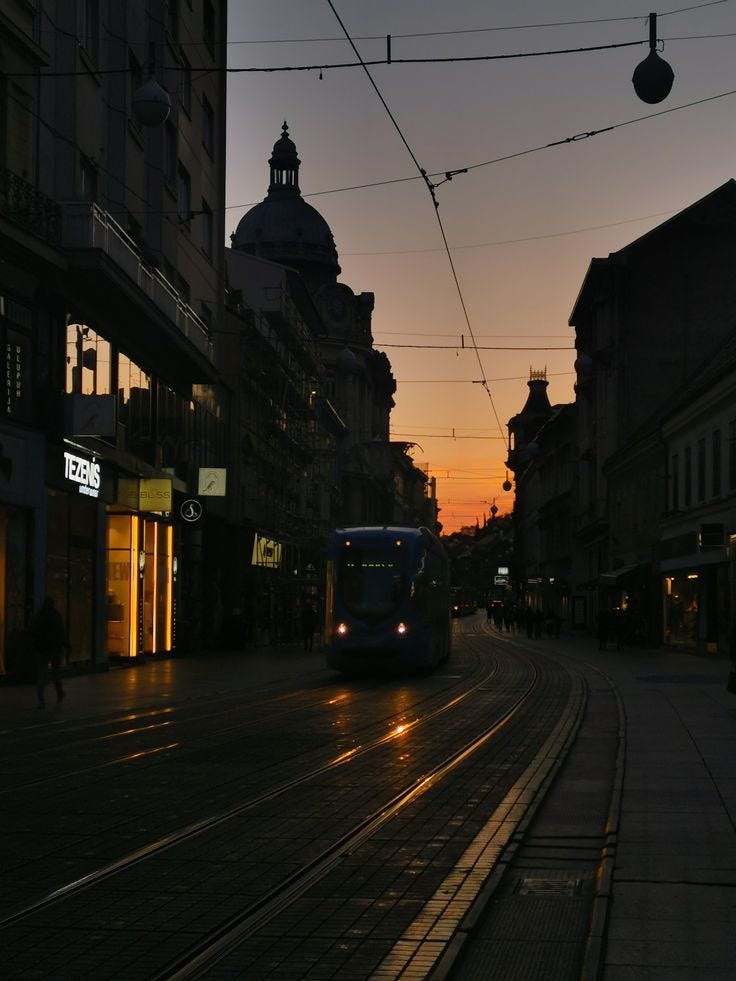 This may contain: a bus driving down a street next to tall buildings at night with the sun going down