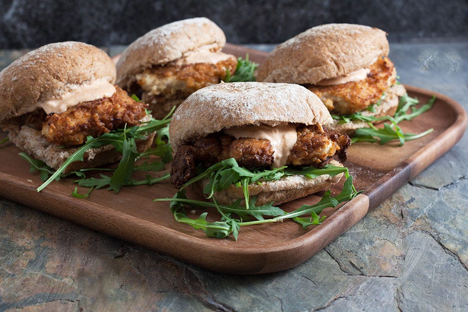 4 fried chicken sandwiches on a wooden tray.