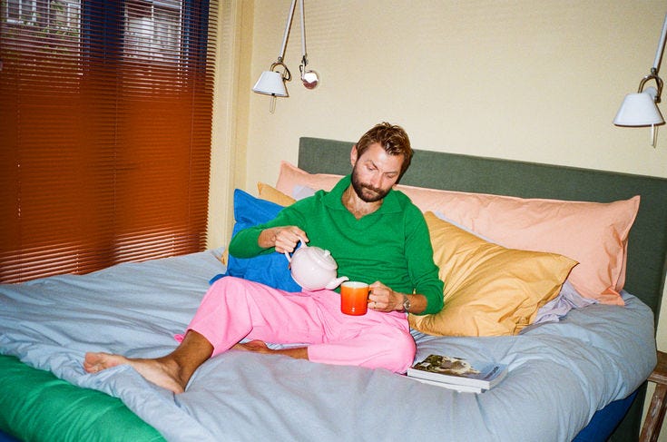 This may contain: a man sitting on top of a bed holding a drink This may contain: a man sitting on top of a bed holding a drink