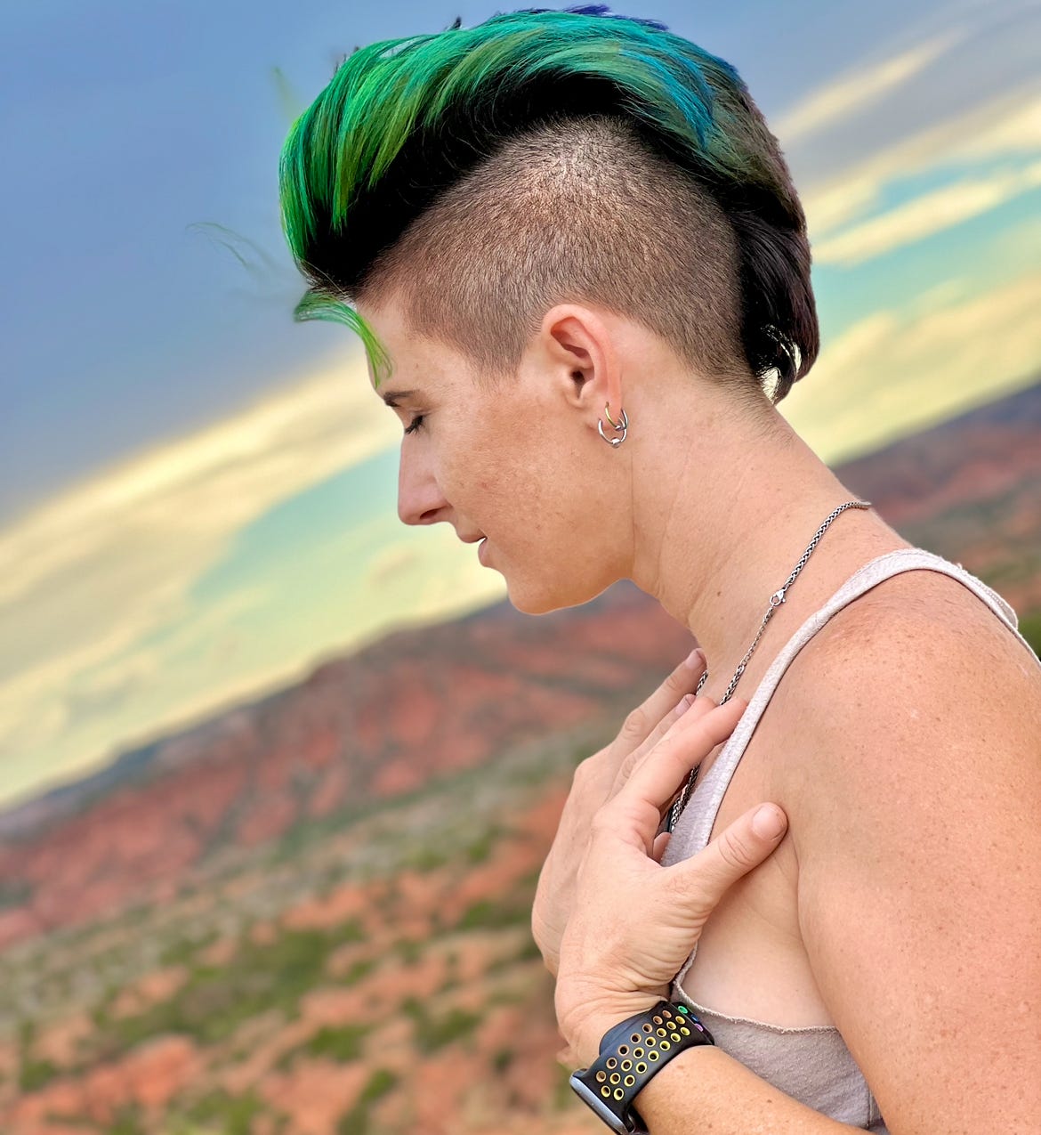 Adult Lyric, with short green hair, and a white tank-top. They stand in the desert as they close their eyes, as if visualizing something. Adult Lyric, with short green hair, and a white tank-top. They stand in the desert as they close their eyes, as if visualizing something.