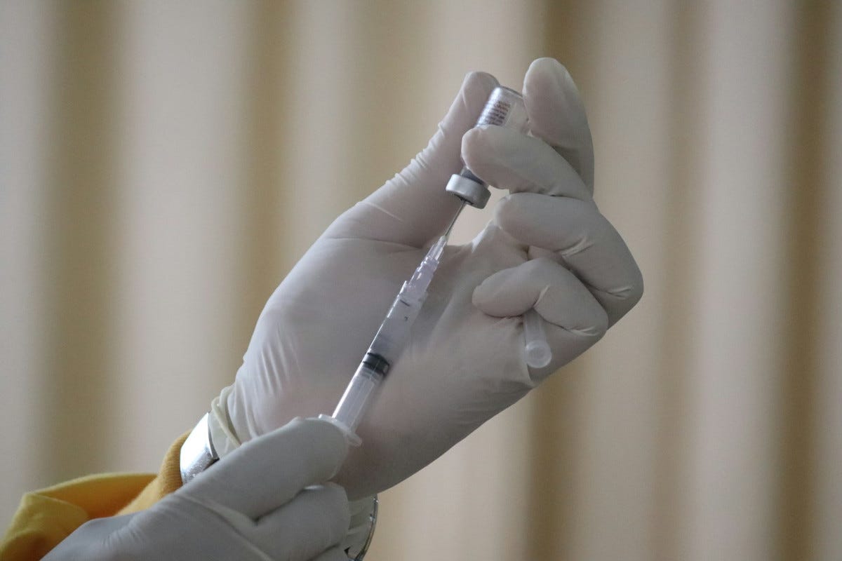 Glove hands use syringe to draw vaccine from a tiny bottle Glove hands use syringe to draw vaccine from a tiny bottle