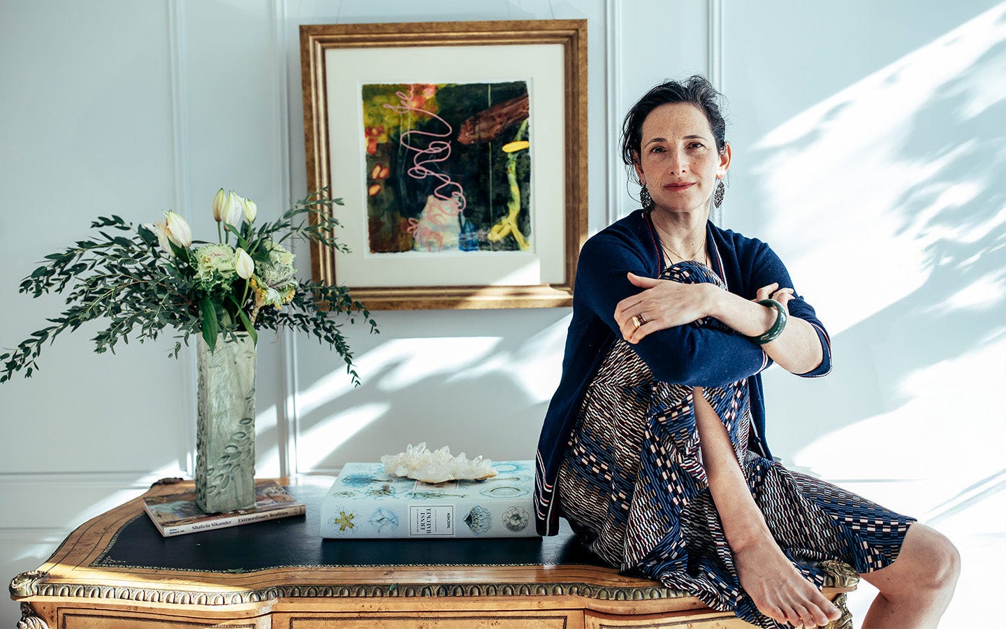 Dr. Catherine sitting on a table with a vase of flowers and framed artwork in the background