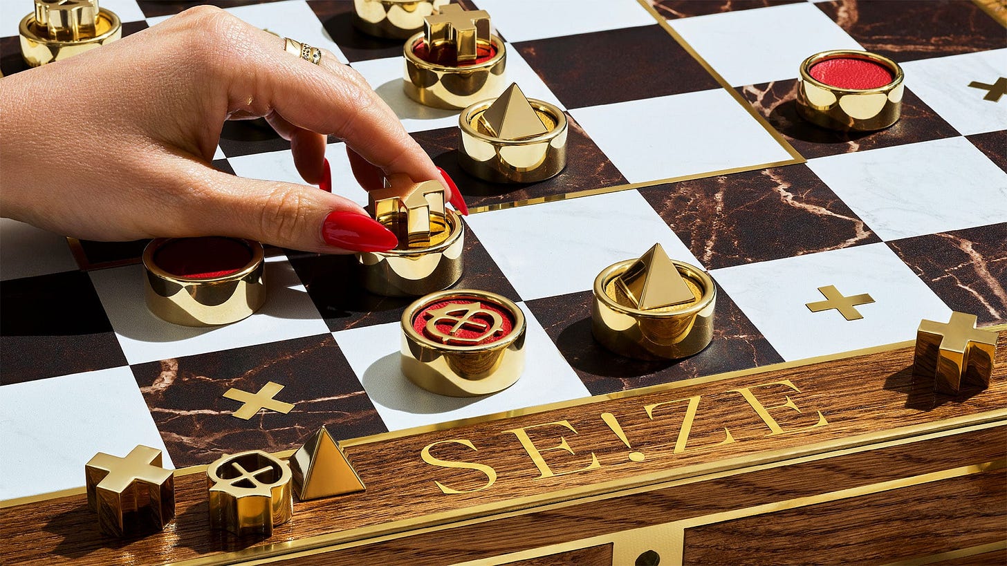 A close-up shows a manicured hand with red nails moving a gold chess piece on a marble-patterned board, with other polished gold pieces arranged nearby and the word “SEIZE” engraved on the wooden edge. A close-up shows a manicured hand with red nails moving a gold chess piece on a marble-patterned board, with other polished gold pieces arranged nearby and the word “SEIZE” engraved on the wooden edge.