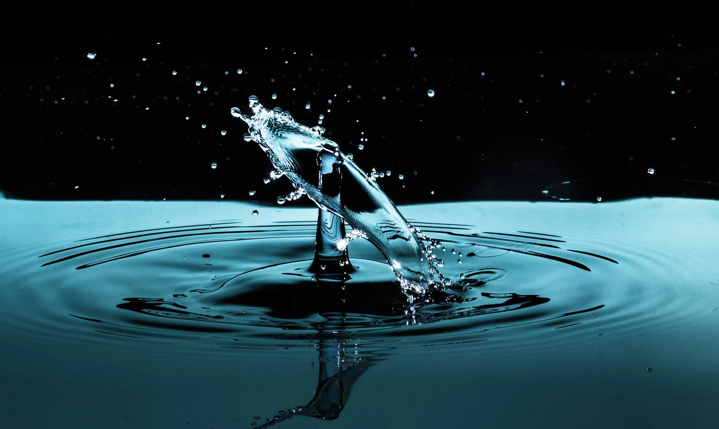 Superficie azzurra di acqua che occupa metà dell'immagine, mentre la parte alta è uno sfondo nero. Dall'acqua emerge una colonna 'd'acqua e una corona di spruzzi di goccioline. Superficie azzurra di acqua che occupa metà dell'immagine, mentre la parte alta è uno sfondo nero. Dall'acqua emerge una colonna 'd'acqua e una corona di spruzzi di goccioline.