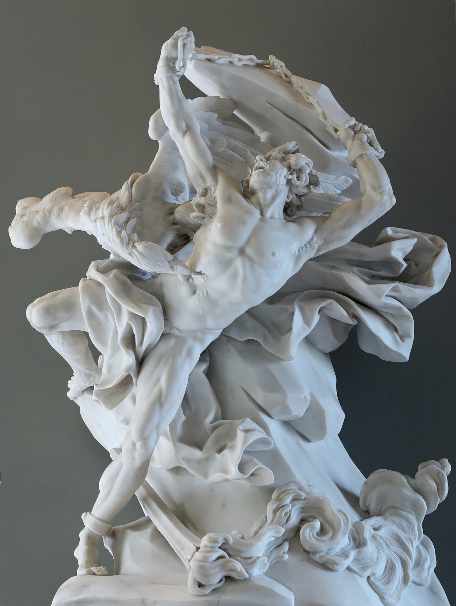 A white marble group: a naked man twists backward on a rock, one arm chained above his head, while an eagle with spread wings tears at his side among swirling folds of drapery.