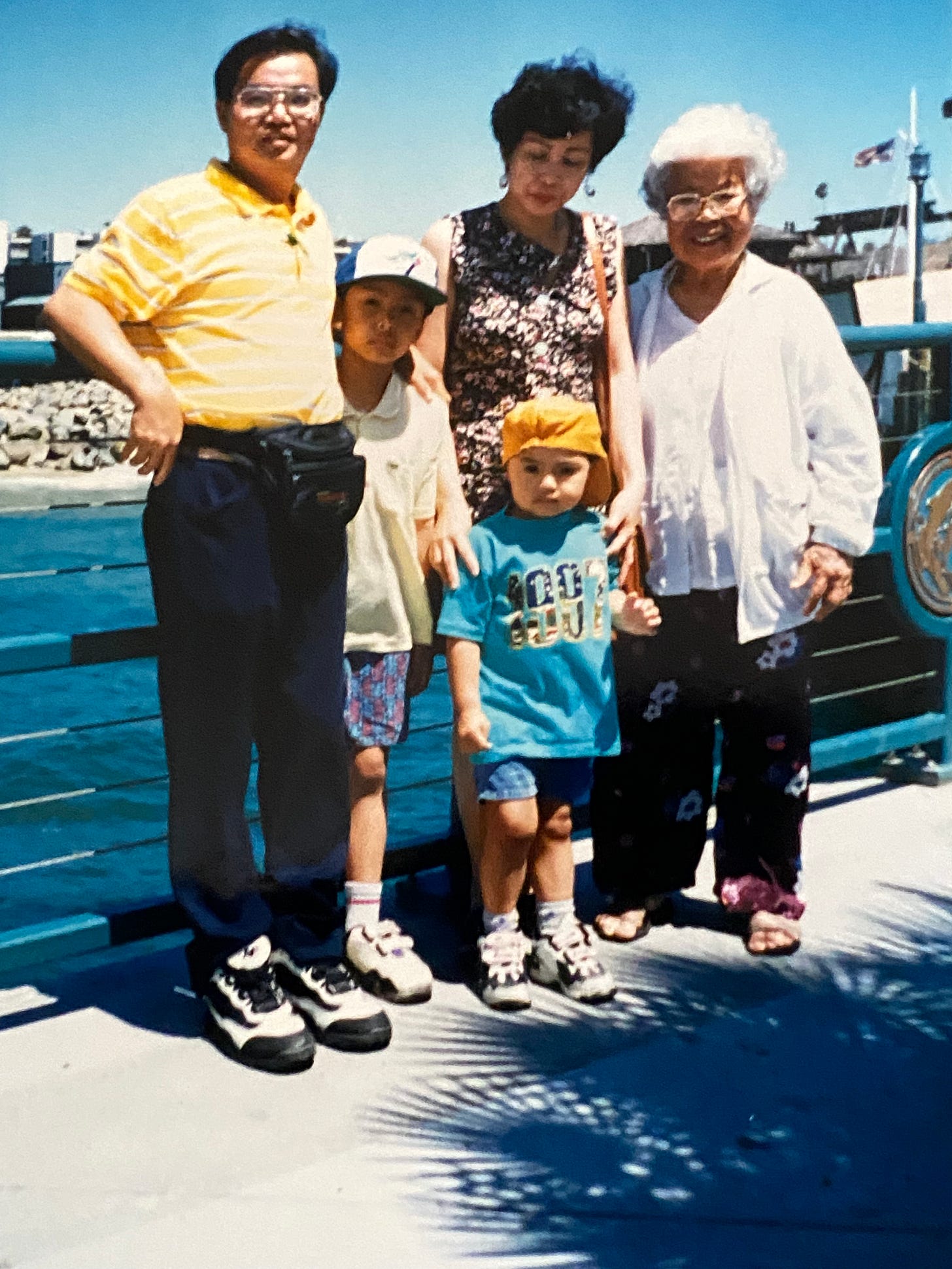 Five people, including young Dennis and family stand close together on a pier by the water. The group appears relaxed and casually dressed, with boats and a bright blue sky in the background. Five people, including young Dennis and family stand close together on a pier by the water. The group appears relaxed and casually dressed, with boats and a bright blue sky in the background.