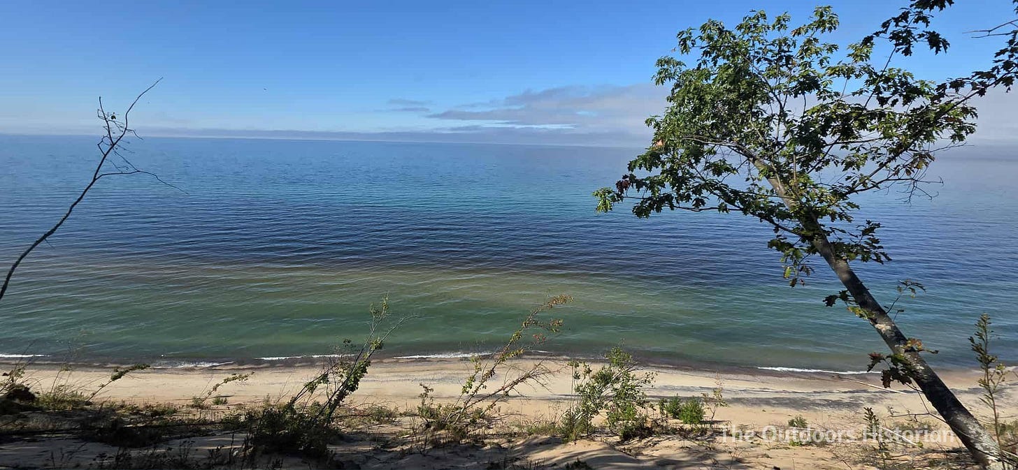 Looking over the dune edge at blue skies, blue water, and a sandy beach.
