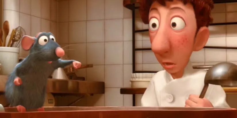 A young cook in a white chef's coat and tall hat stands in a busy restaurant kitchen, looking down with a focused, uncertain expression.