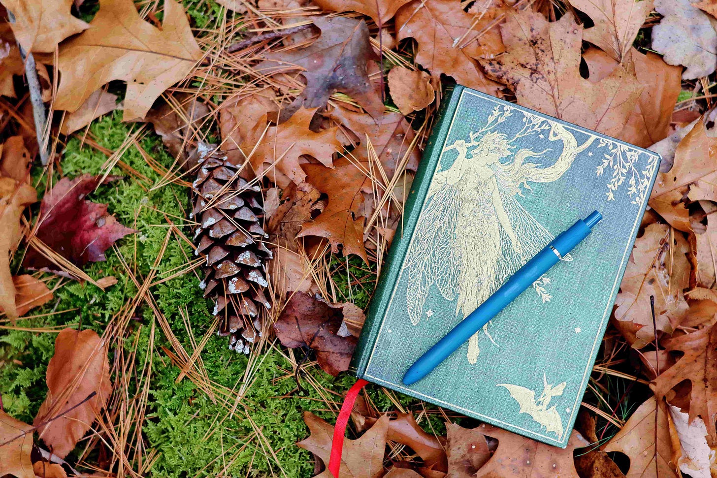 green journal with fairy, pen and leaves on the ground