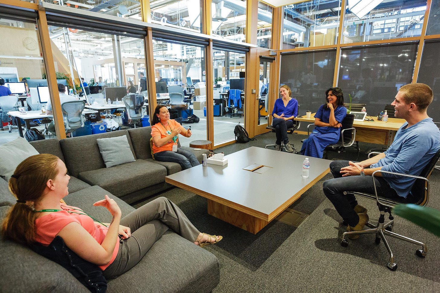 Three white women, a white man, and Deepti, an Indian woman, sit in a plush conference room with glass walls and an open office in the background. Three white women, a white man, and Deepti, an Indian woman, sit in a plush conference room with glass walls and an open office in the background.