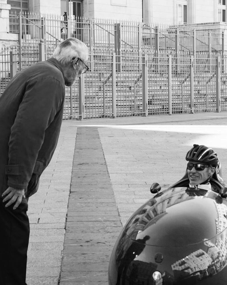 greyscale photography of man standing beside man sitting on mobile
