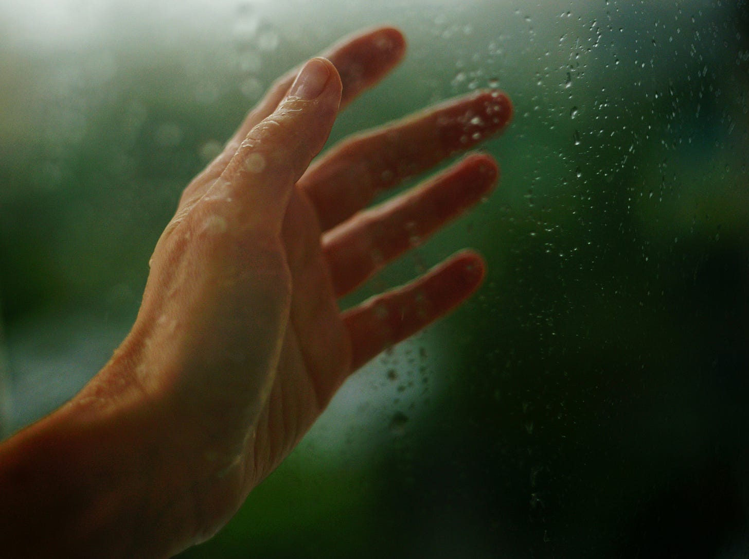 white hand touching rainy windowpane