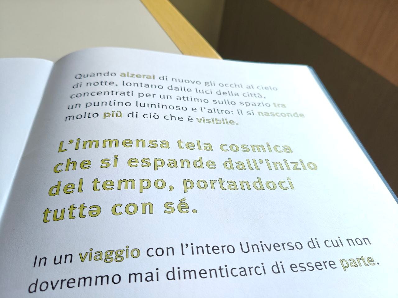 Una pagina della parola SPAZIO delle Scatoline di effequ, con questa scritta: "L'immensa tela cosmica che si espande dall'inizio del tempo, portandoci tuttə con sé". La pagina è appoggiata su un tavolo di legno bianco sporco e nell'angolino in alto a destra si intravede un pezzetto di muro in ombra.