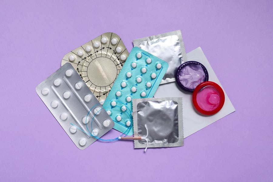 Contraceptive pills, condoms and an intrauterine device laying on a violet background.