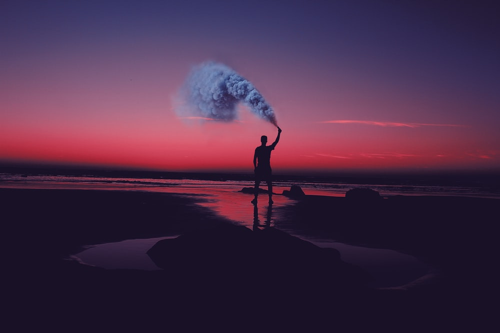 silhouette of man standing on seashore holding smoke can silhouette of man standing on seashore holding smoke can