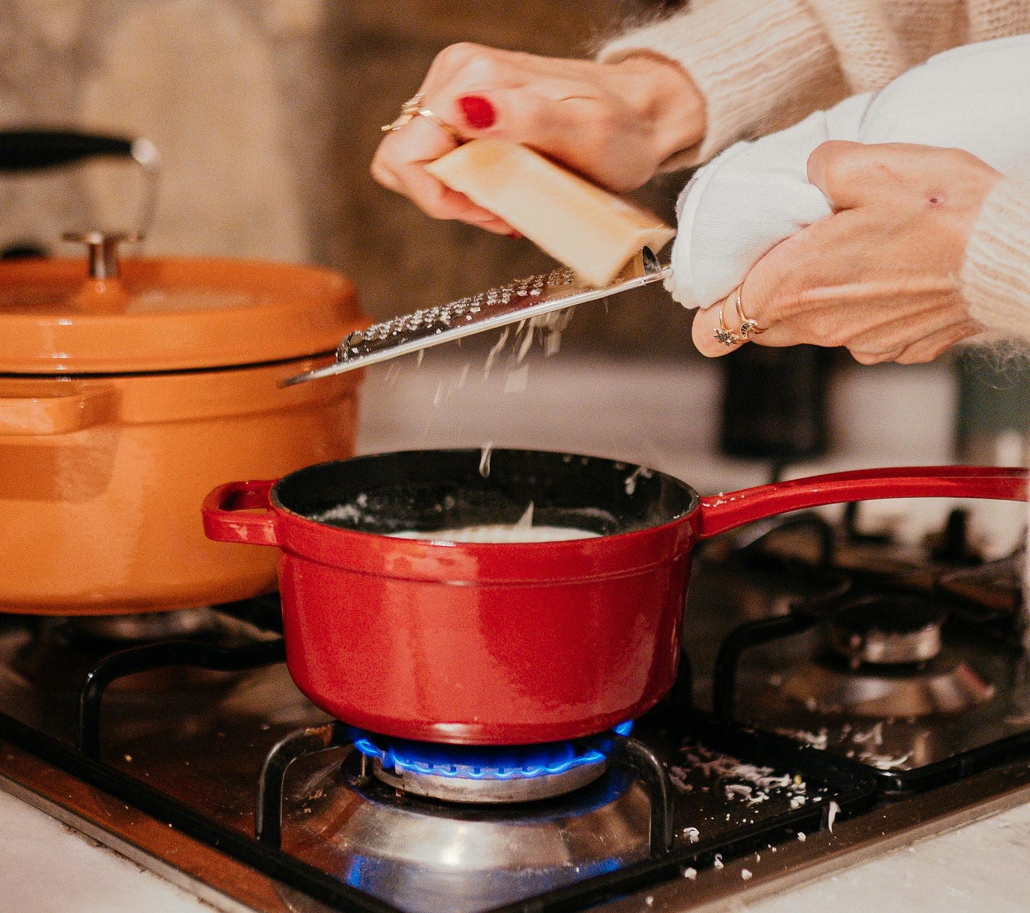 person shredding cheese into pot on stove person shredding cheese into pot on stove