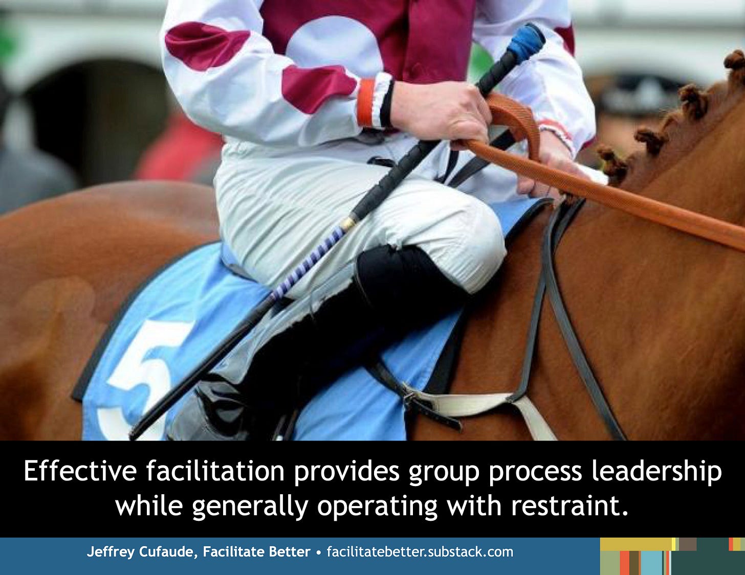 closeup of a jockey atop a stationary race horse with one hand holding both the bridle and a riding crop