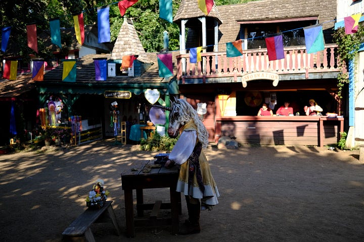 Bards singing in a tavern wearing medieval garb, an elf and wizard surveying goods at a shop, fire-twirler show, Geralt and another warrior deep in conversation, a man playing dead with an arrow under his armpit, guests walking toward the camera, a woman with a horse head looking over a table.