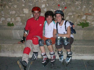 Me, center, with two friends.  We are wearing helmets and rollerblades and sitting on a curb with a stone wall behind us.