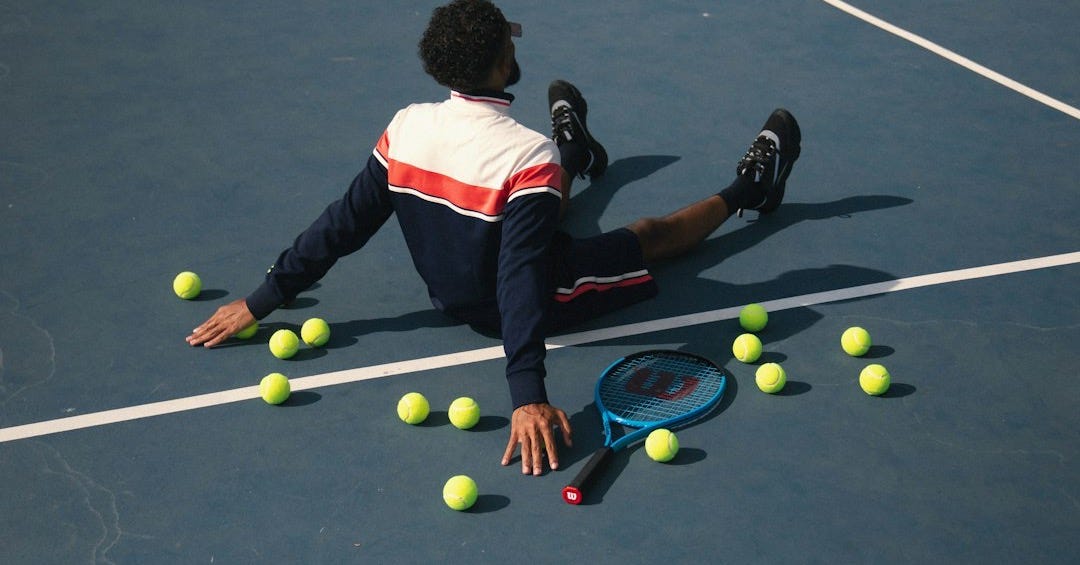 A man laying on a tennis court surrounded by tennis balls A man laying on a tennis court surrounded by tennis balls