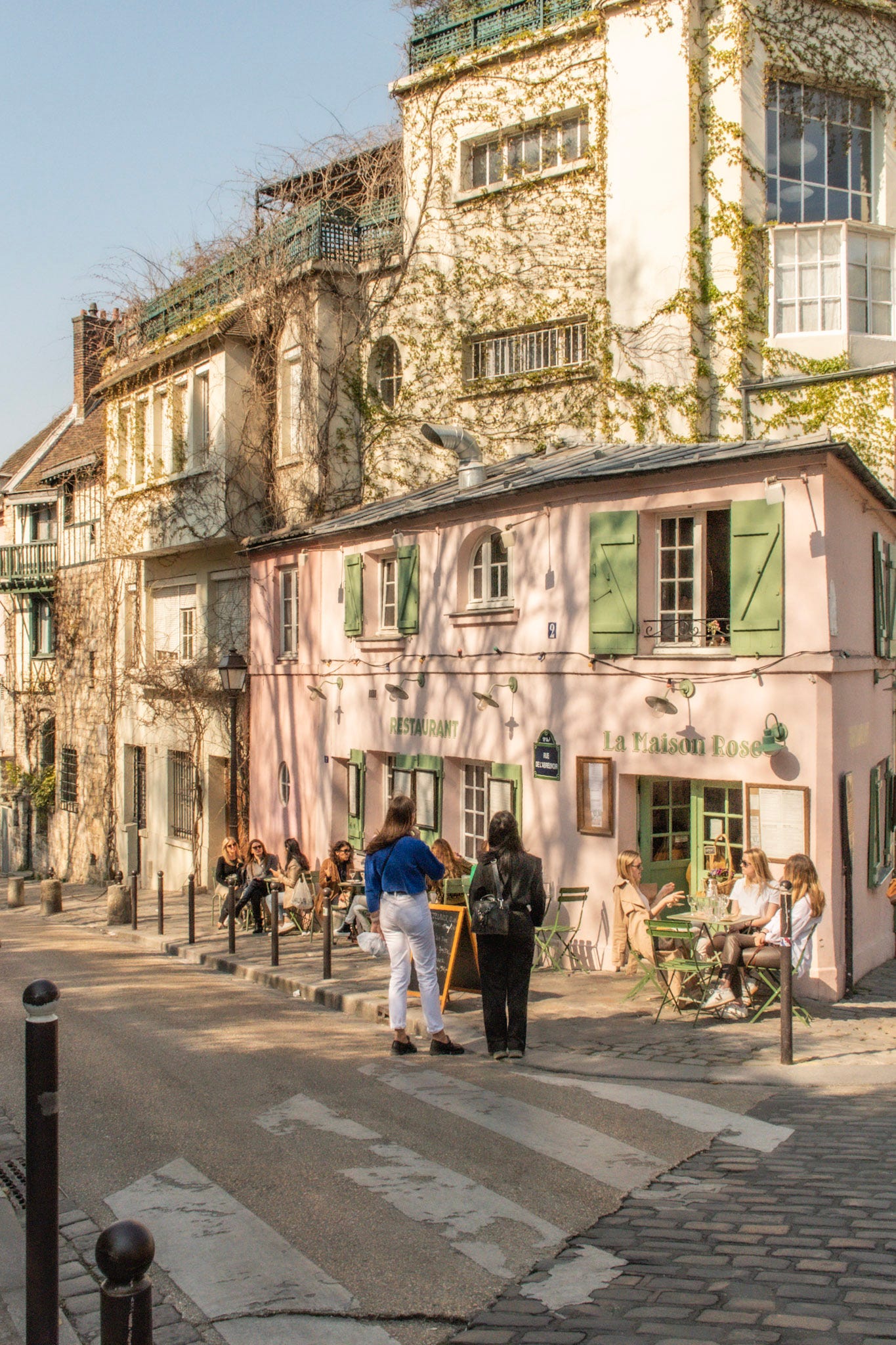 La Maison Rose café on Rue de l'Abreuvoir in Montmartre, with its pastel pink façade, green shutters and outdoor café tables.