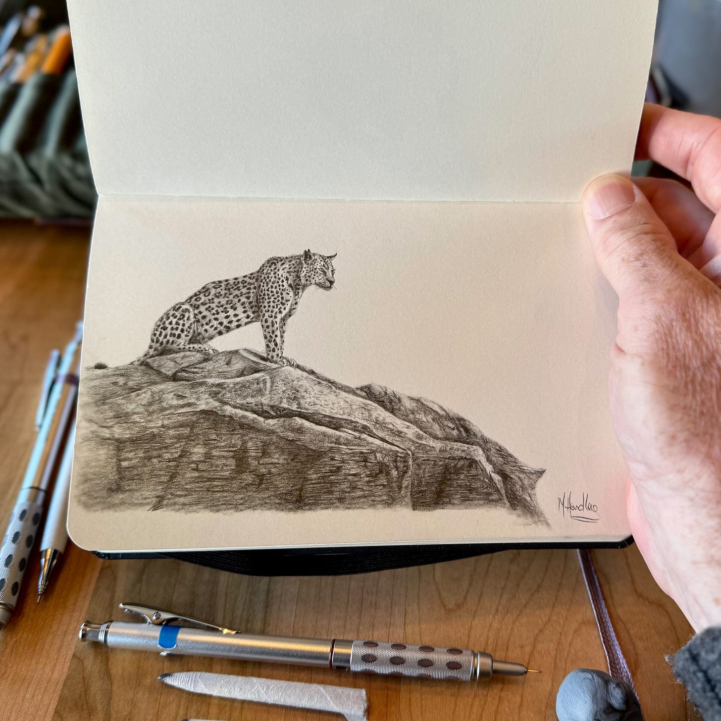 A drawing of a leopard in a sketchbook surrounded by pencils