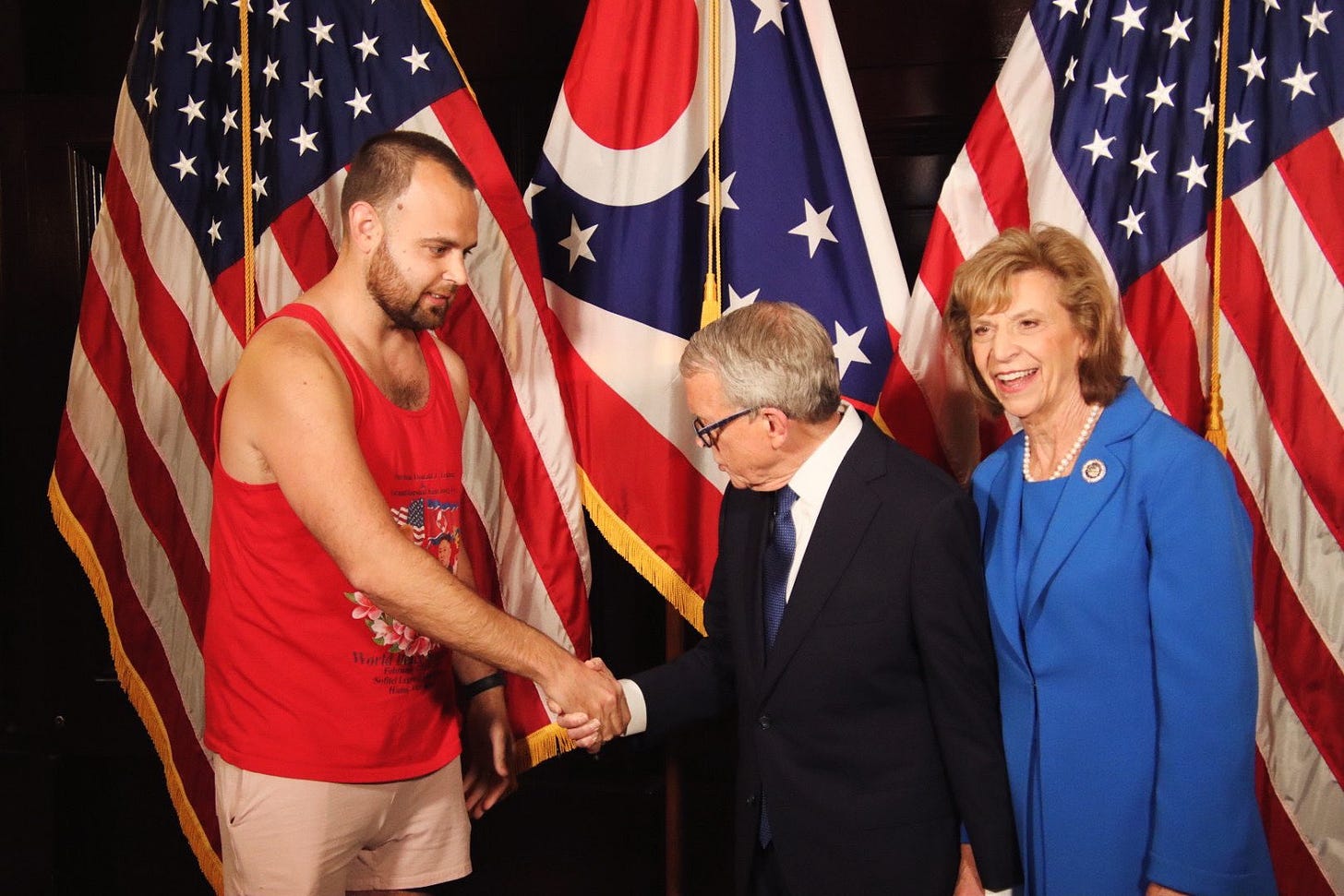 Image D.J. Byrnes, owner and operator of The Rooster, shakes hands with Ohio governor Mike DeWine while his wife, Fran, looks at reporters.