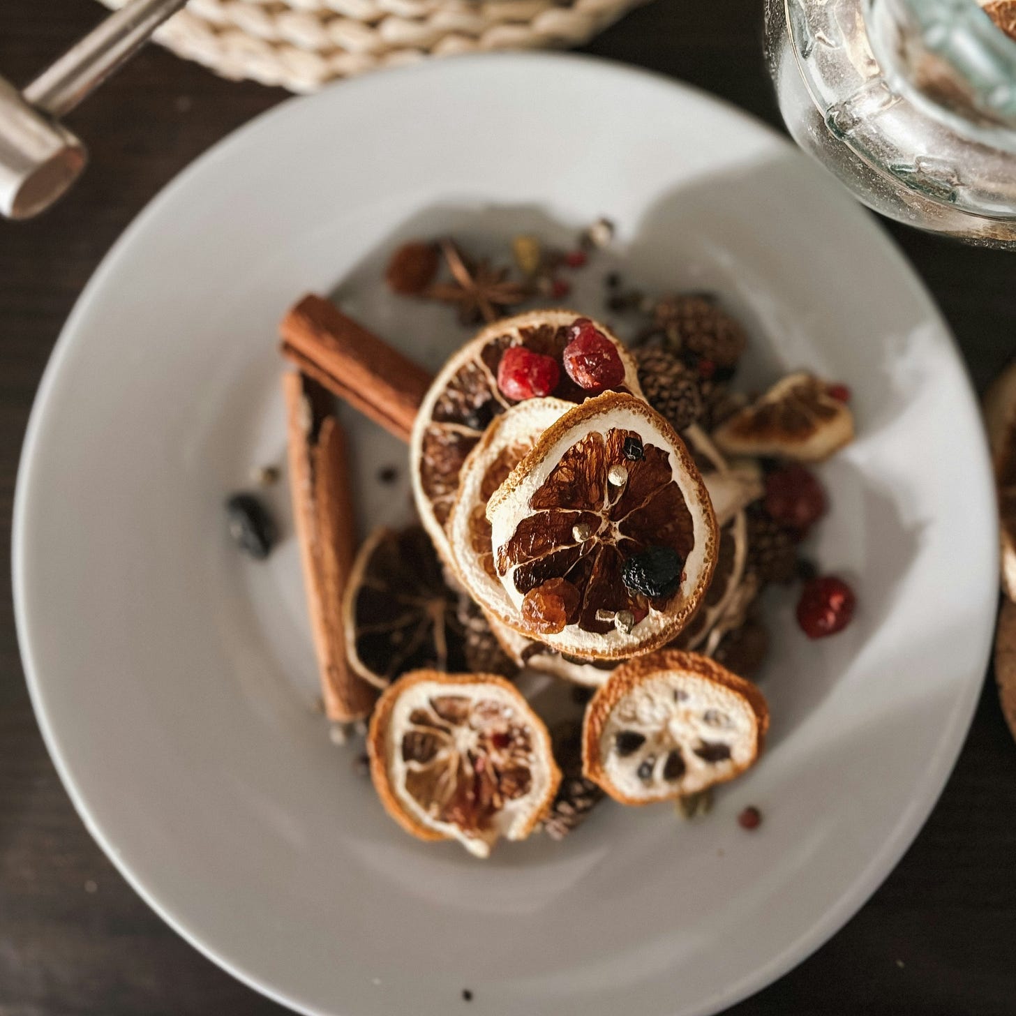 Upon a white plate are a scattering of festive spices -- cinnamon sticks, star anise, dried orange slices, raisins, and cranberries.