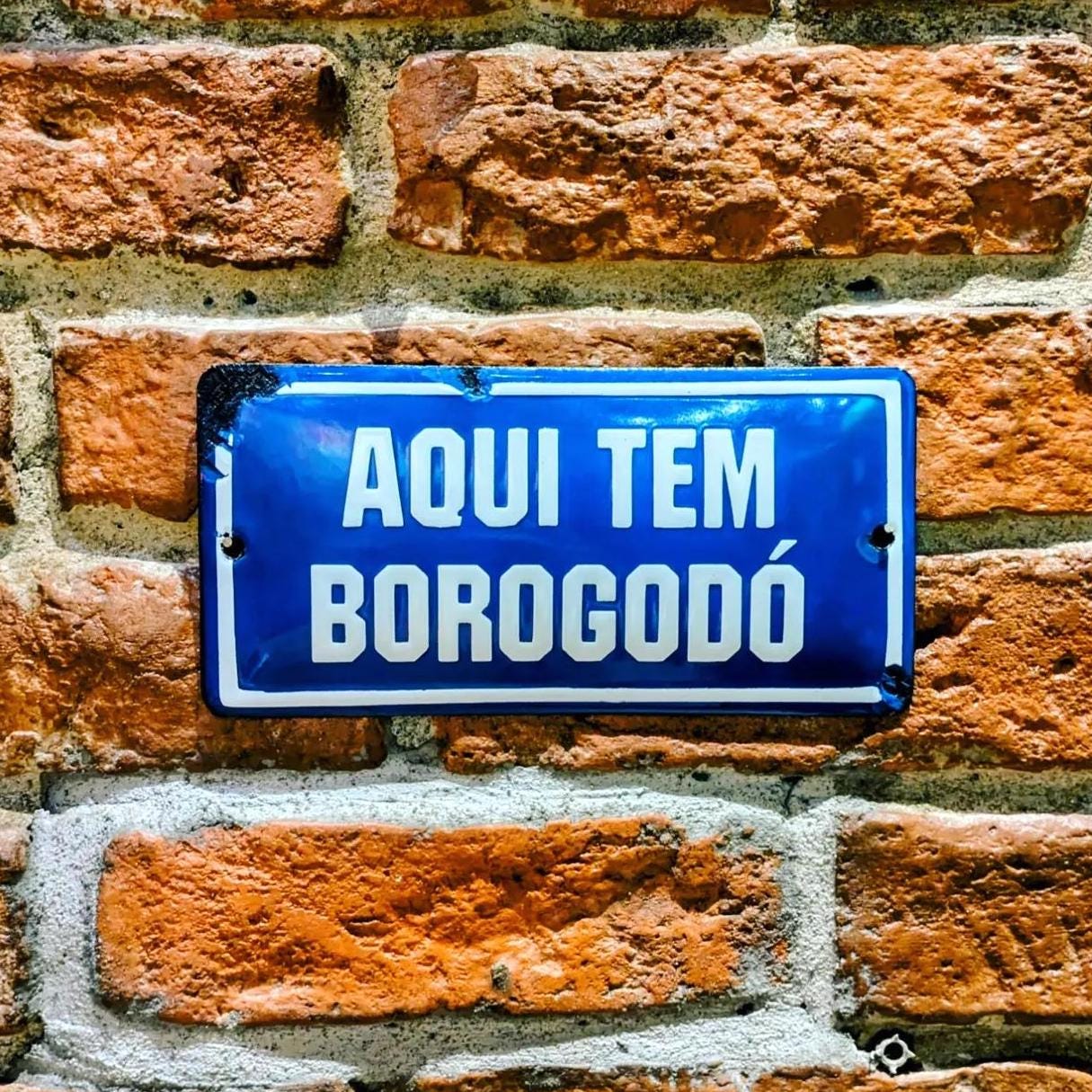 A brick wall with a blue plaque saying "Aqui tem borogodó" [there's borogodó here].