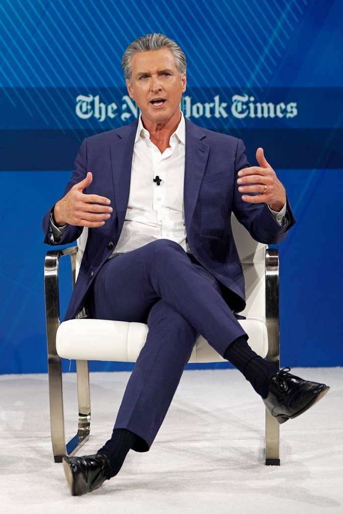 Person in a suit seated on a stage, speaking animatedly with hands gesturing, at a New York Times event Person in a suit seated on a stage, speaking animatedly with hands gesturing, at a New York Times event