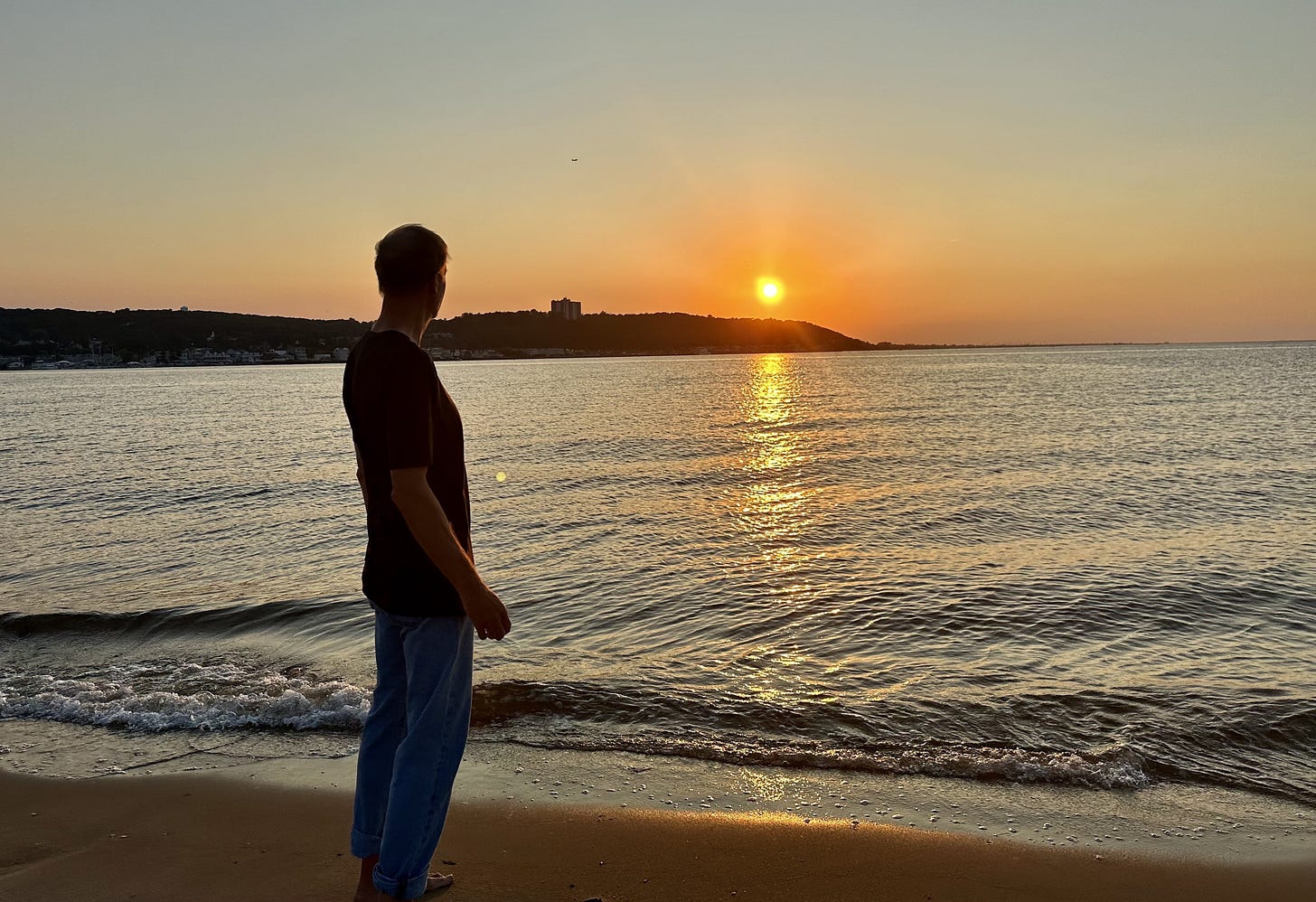 Man standing at edge of bay watching the sun set. 